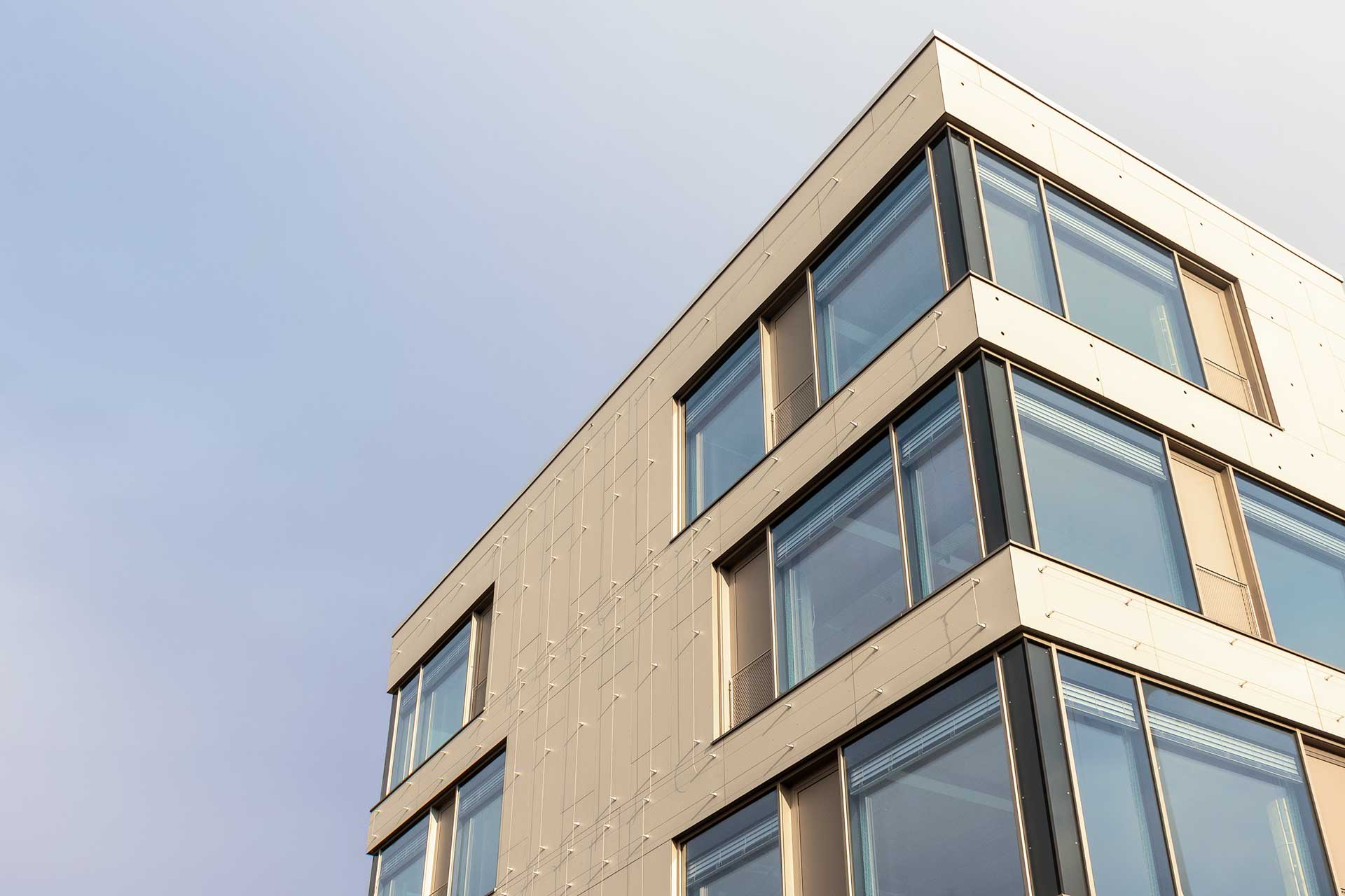 Außenansicht eines ooberen Gebäudeteils mit Flachdach und breiten Eckfenstern.