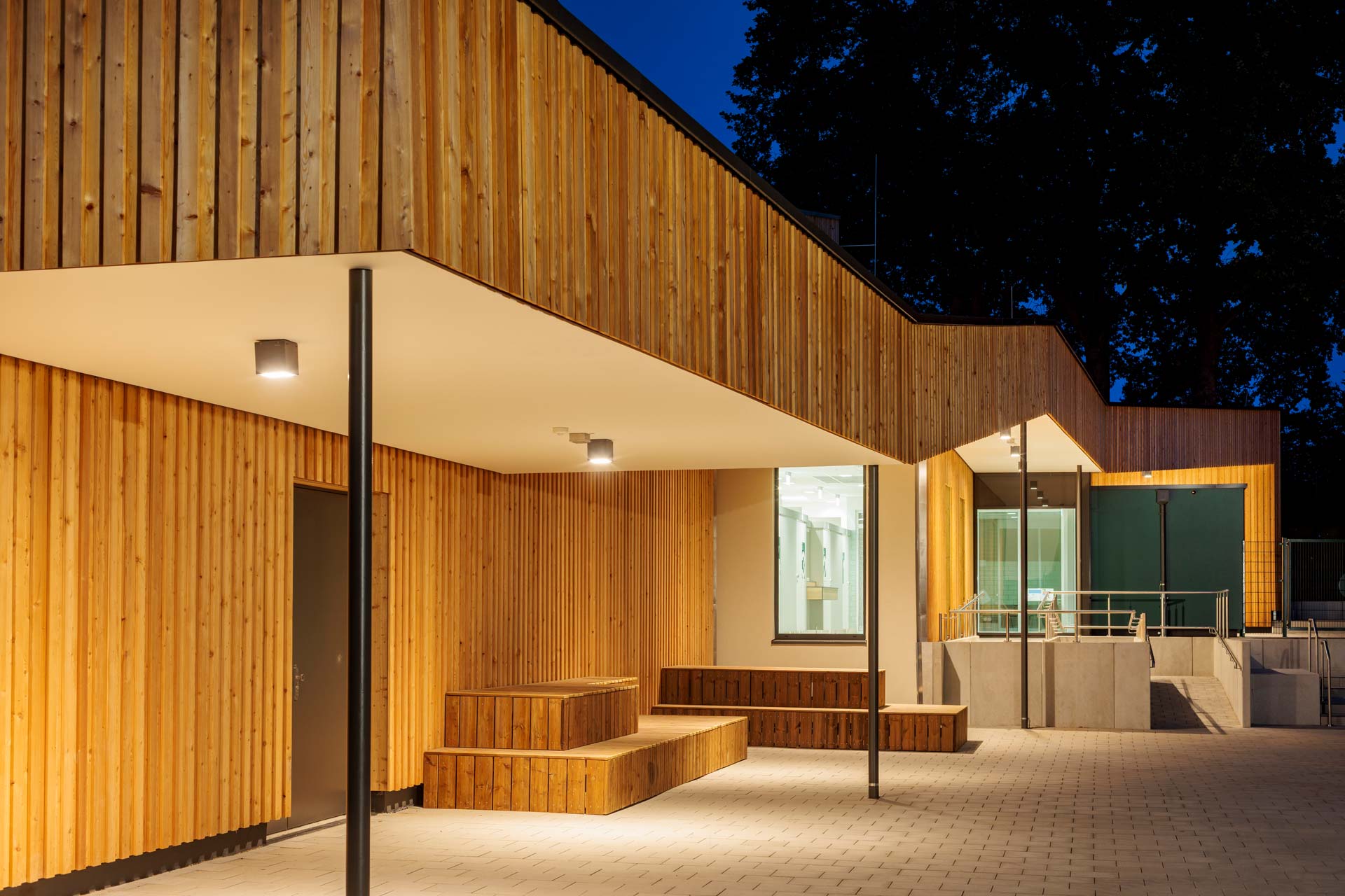 Beleuchtetes holzverkleidetes Geb&auml;ude mit Flachdach.