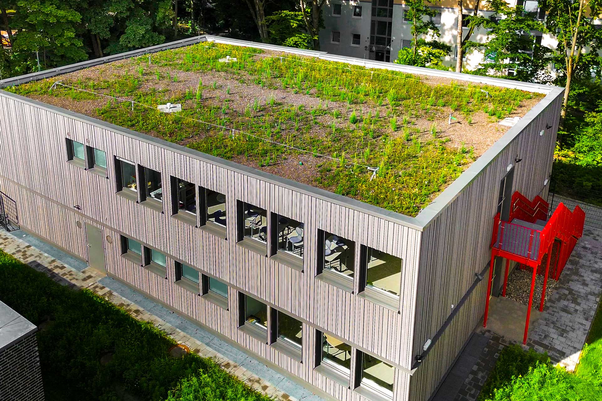 Modulbauschule in Holzoptik mit einer roten Außentreppe.