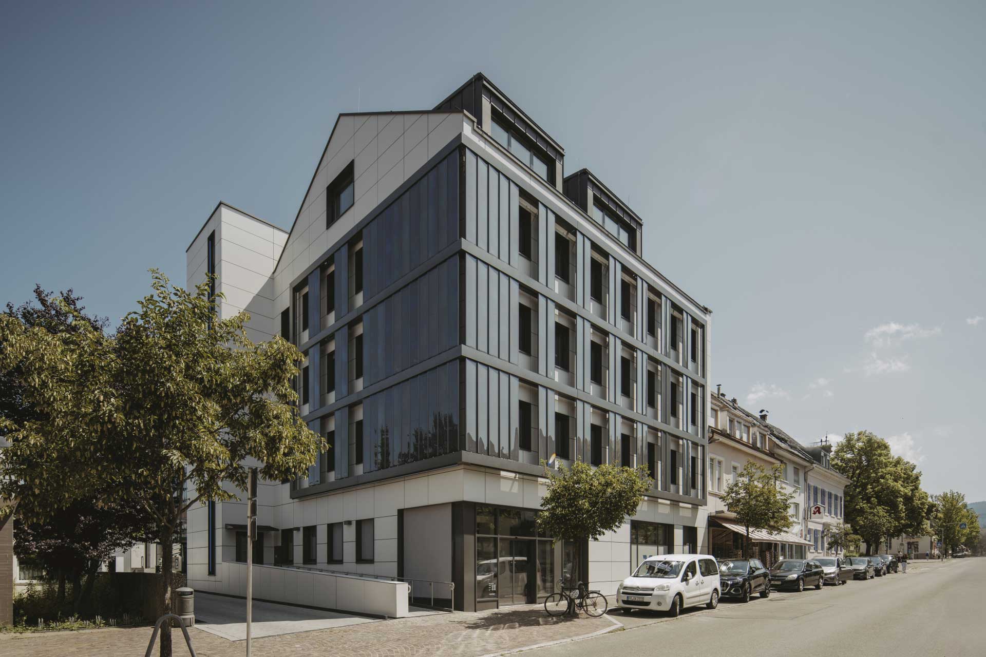 Eckansicht eines Gebäudes mit heller und dunkler Fassade an einer Straße.