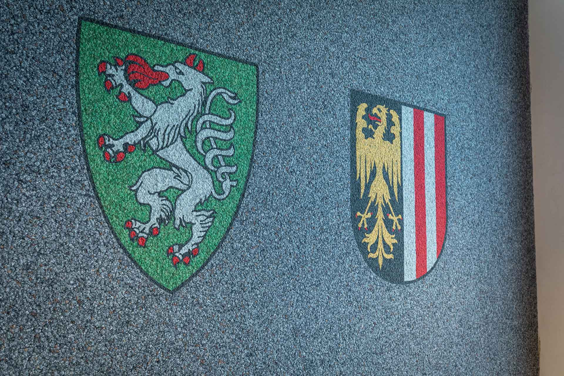 Wappen der Bundeslänger Oberösterreich und Steiermark an einer Wand.