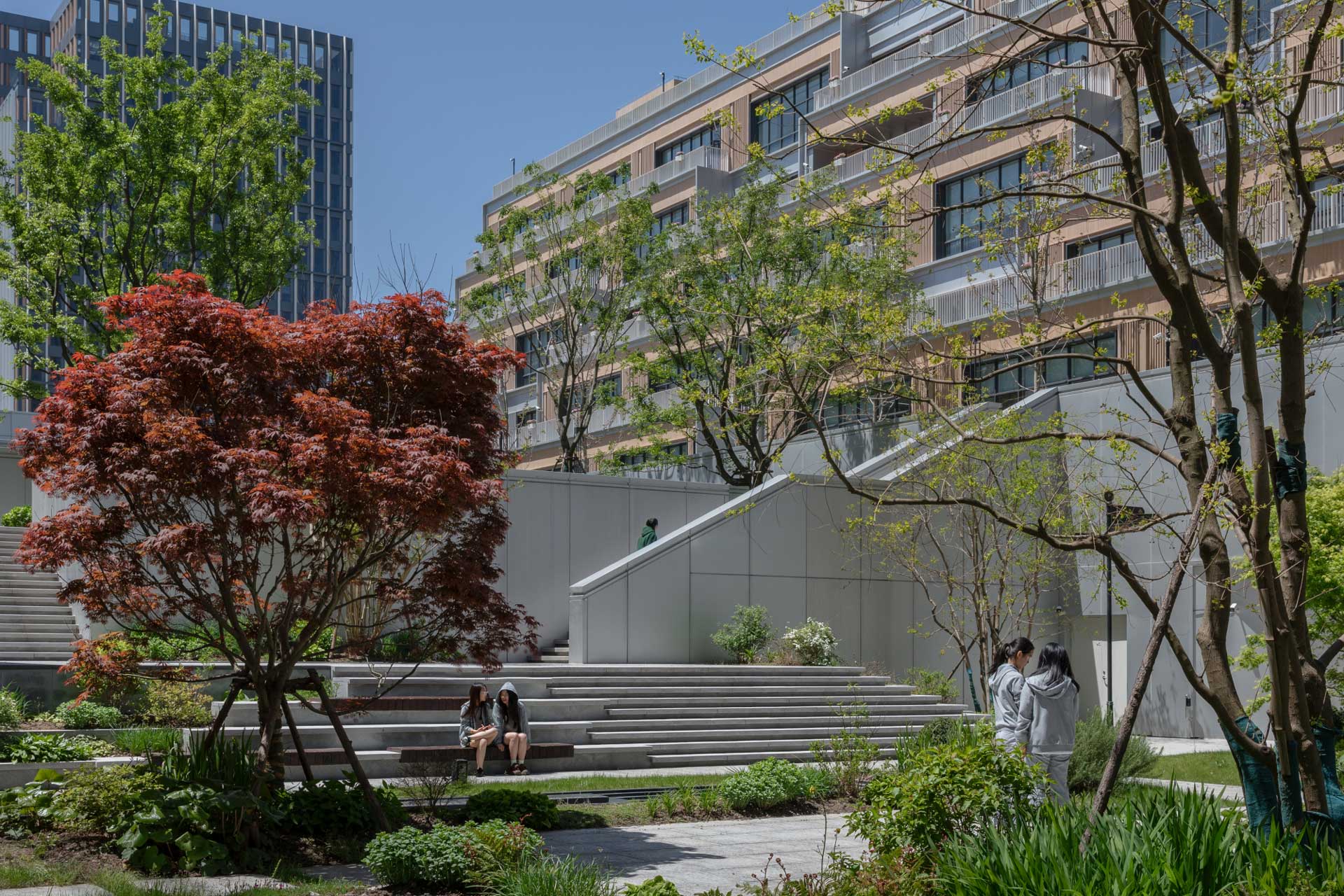 Green courtyard between two apartment buildings. Two women are sitting on stone steps. 