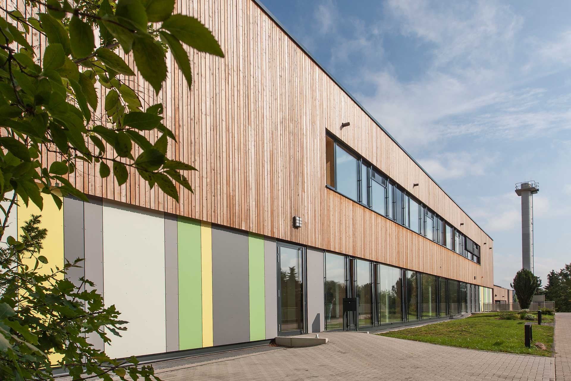 Gebäude mit Flachdach. Im oberen Stock ist die Fassade mit Holz verkleidet, unten mit bunten Platten.