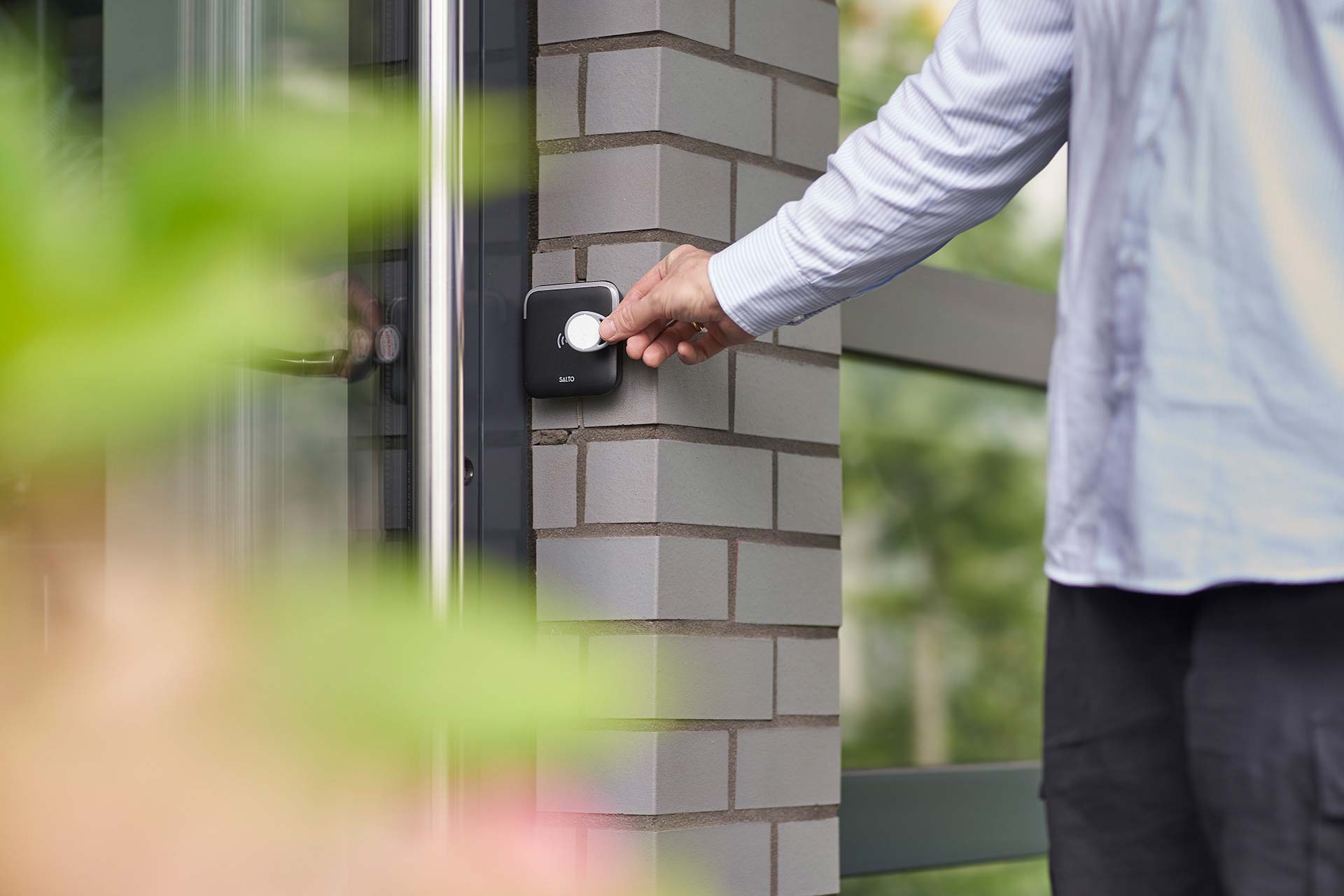 Haustür mit elektronischem Türöffner. Eine Hand hält einen Token daran.