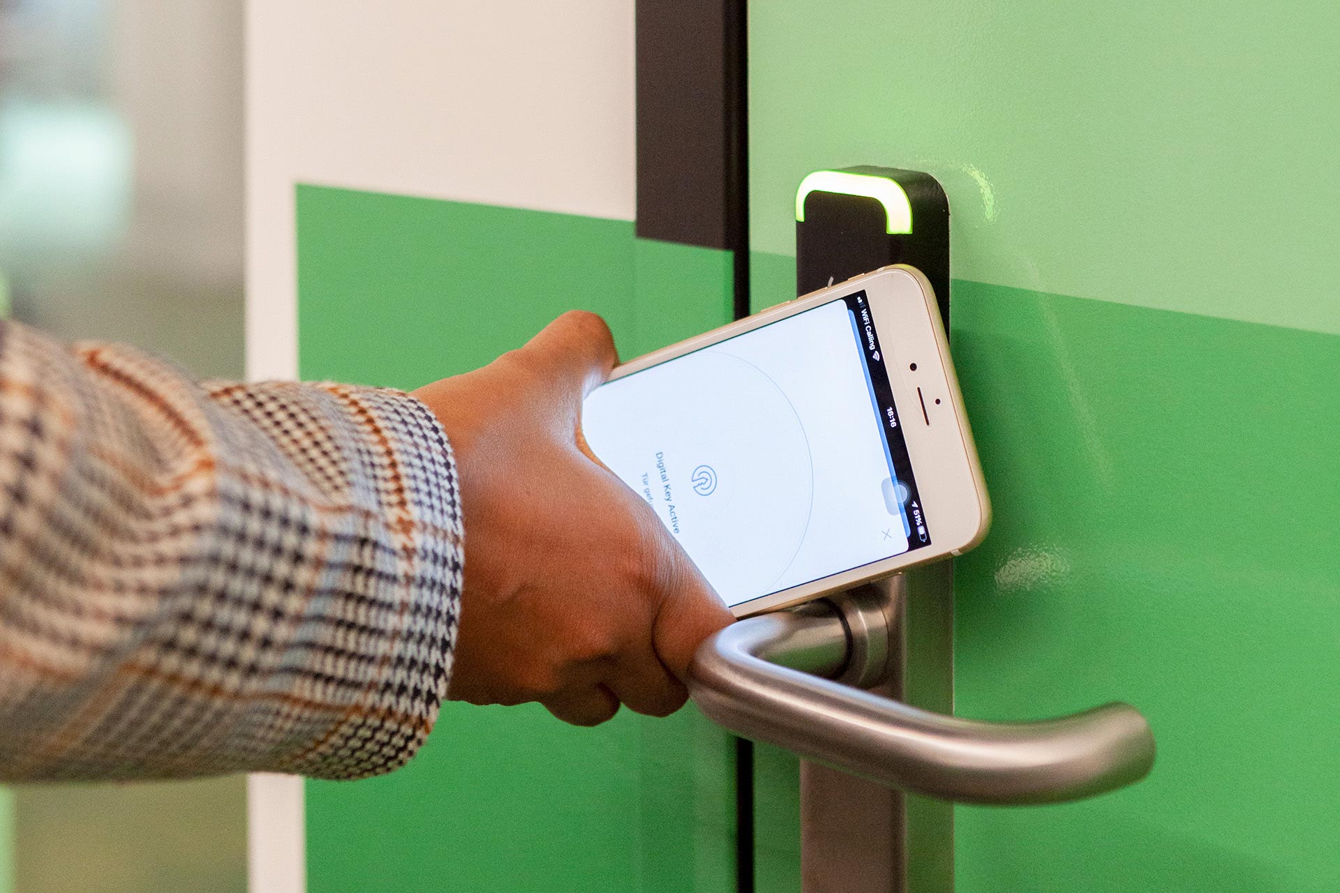 Eine Hand h&auml;lt ein Handy an einen T&uuml;rgriff.