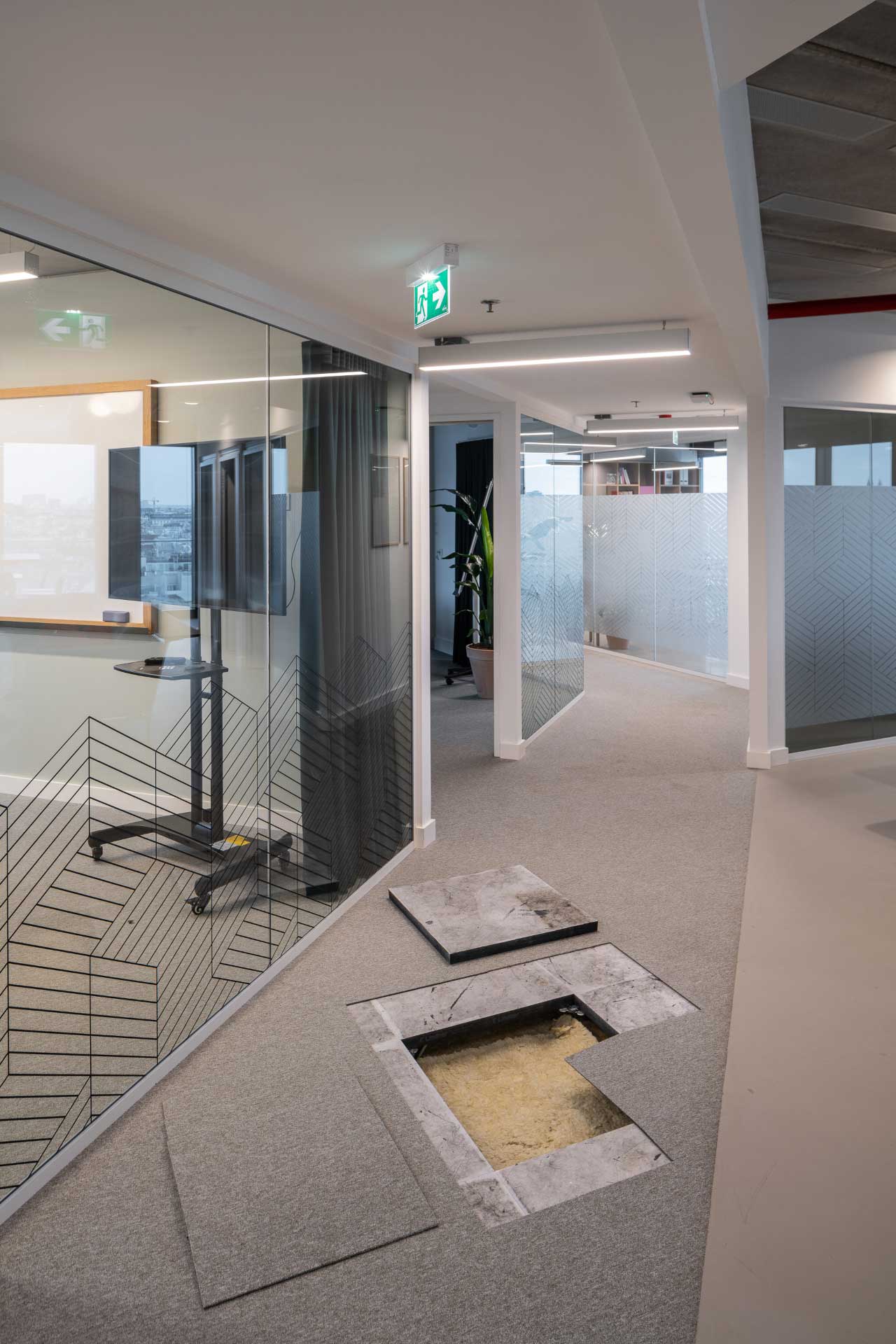 Büroflur mit durch Glas abgetrennten Einzelbüros. Im Boden sieht man ein Loch.