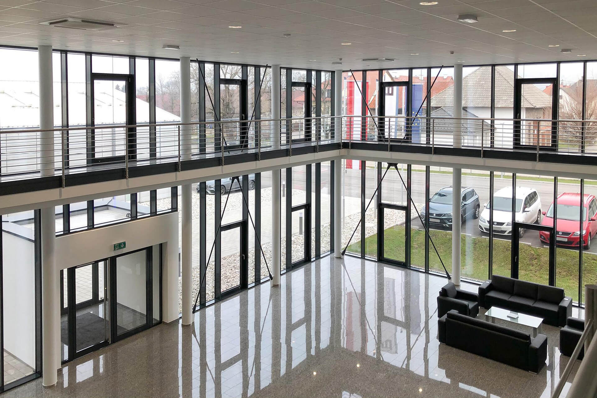 Komplett verglaste Eingangshalle mit schwarzen Sofas als Sitzgelegenheit und hellem Fliesenboden.