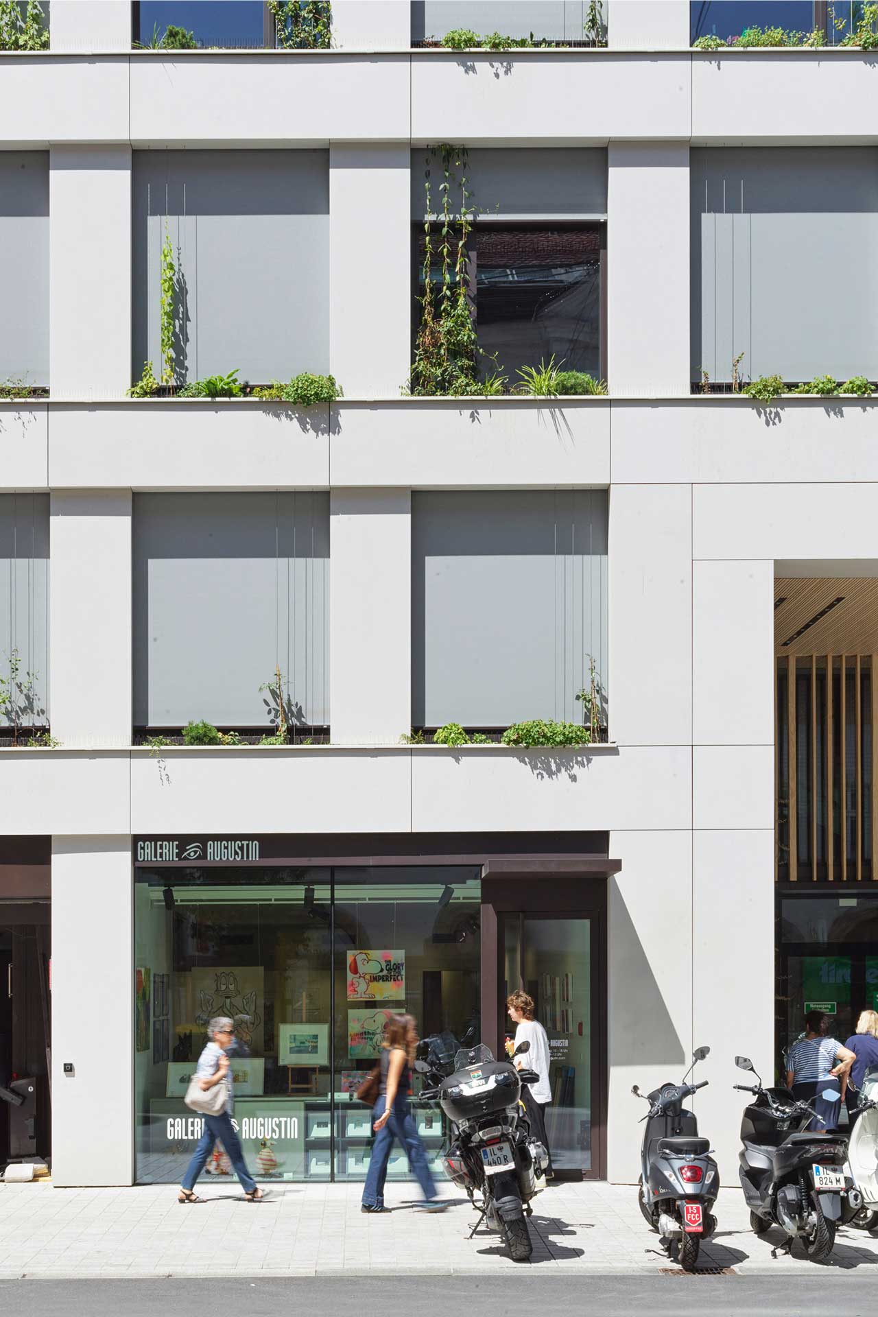 Bürogebäude mit Laden im Erdgeschoss. Davor gehen Menschen auf einem Gehweg vorbei.