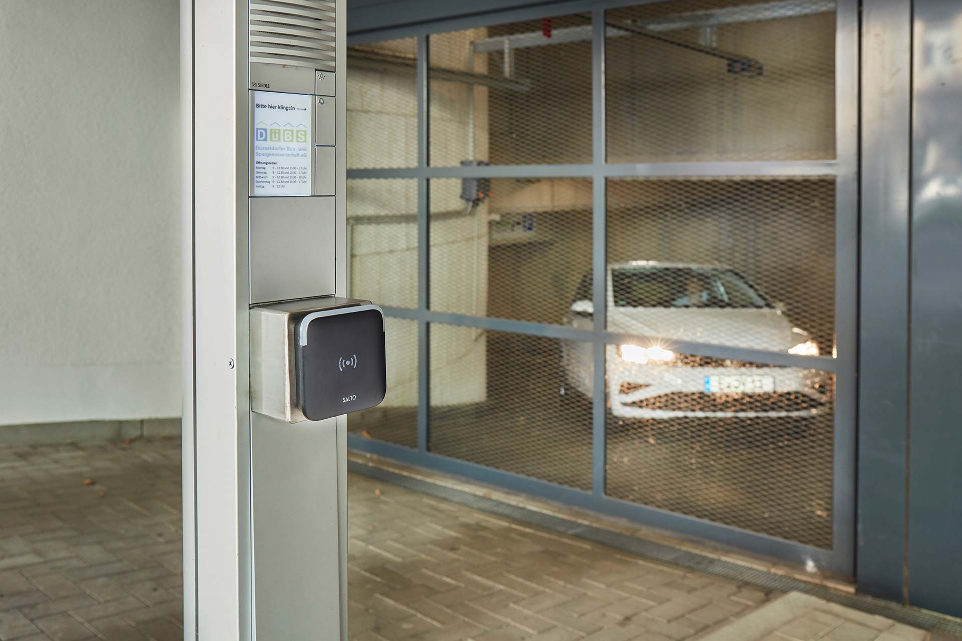 Tiefgarage mit Gittertor, aus der ein weißes Auto herausfahren will.