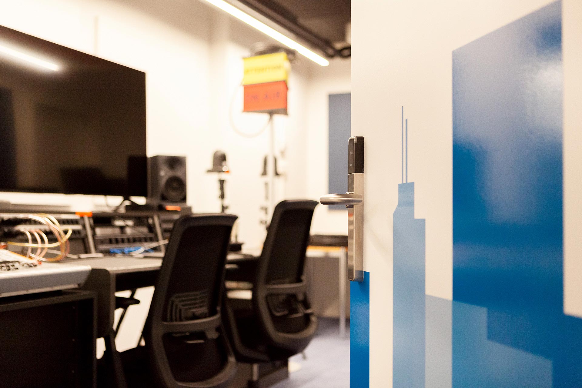 Blick in ein B&uuml;ro mit einem Schreibtisch, zwei St&uuml;hlen und viel Technik auf dem Tisch.