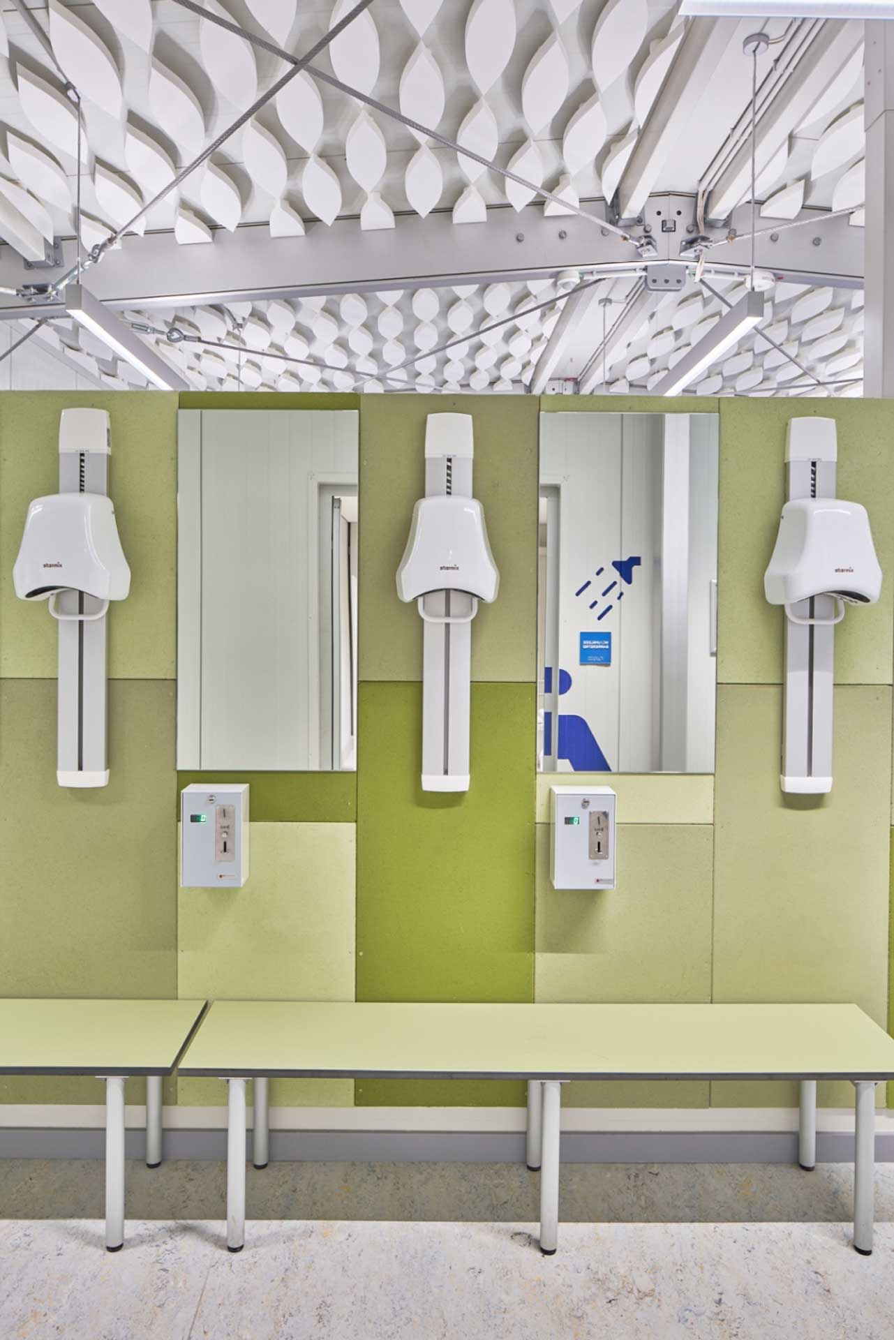 Umkleidebereich eines Schwimmbades mit Spiegeln, Föns und einer Sitzbank.