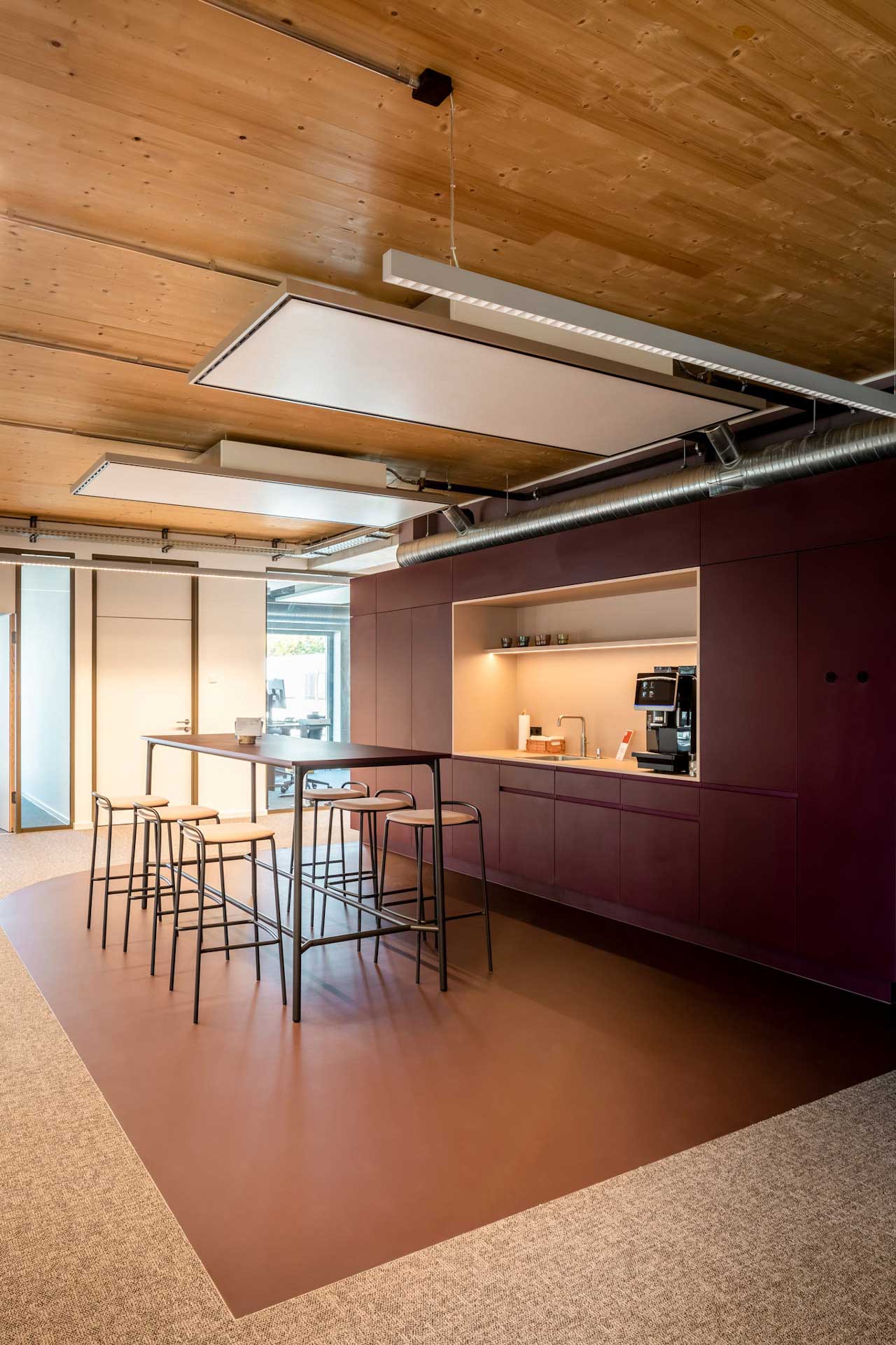 Küchenzeile in einem Büro mit Stehtisch und Stühlen davor.