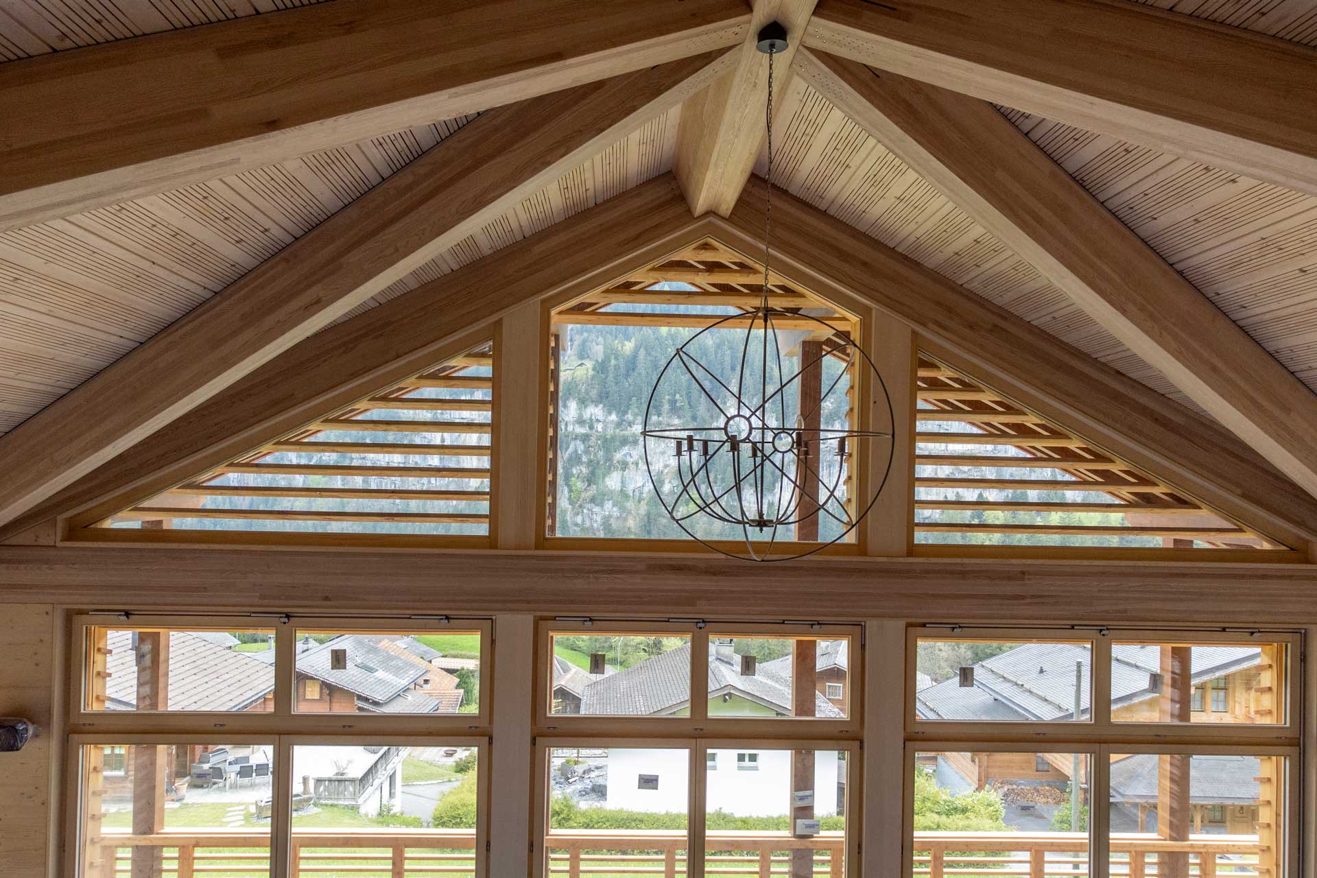 V-förmig zulaufende Holzdecke über einer Fensterfront mit Sprossenfenstern.