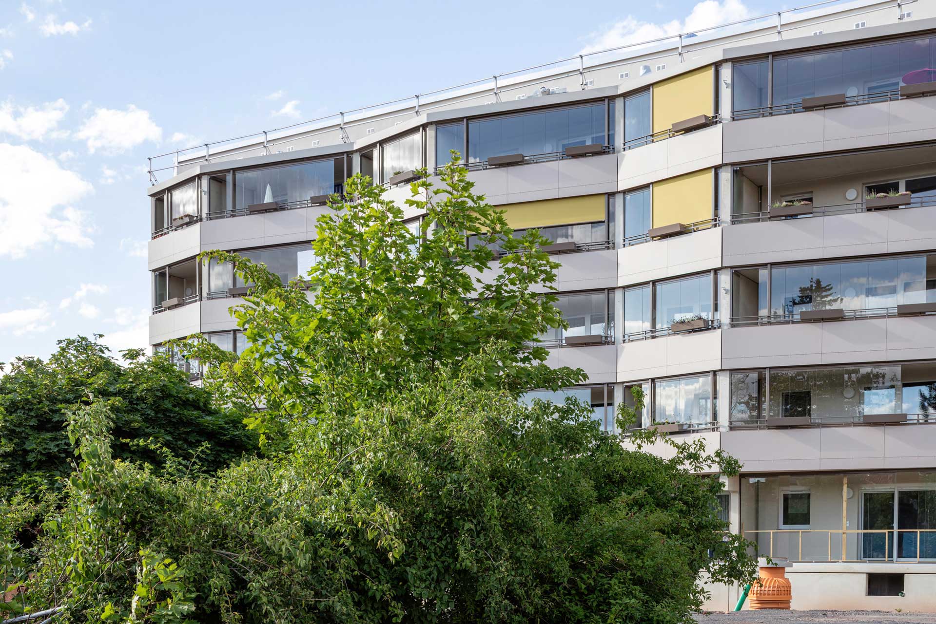 Mehrfamilienhaus mit durchgängigen Loggien und Flachdach. Die Loggien werden teils mit Sonnenschutz verschattet.