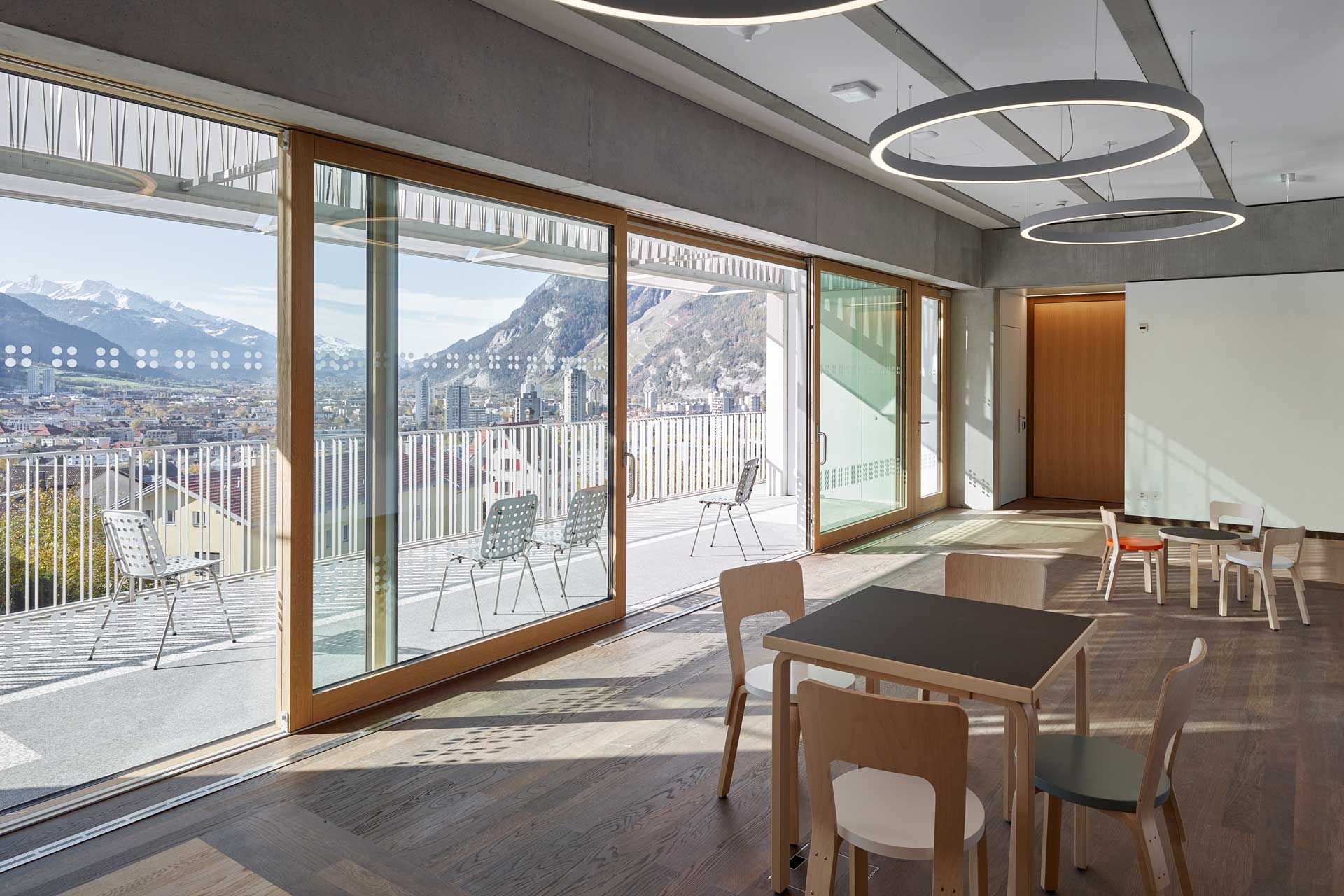 Raum mit Holzparkett und großer Fensterfront. Die Schiebetür ist geöffnet, davor ein breiter Balkon.