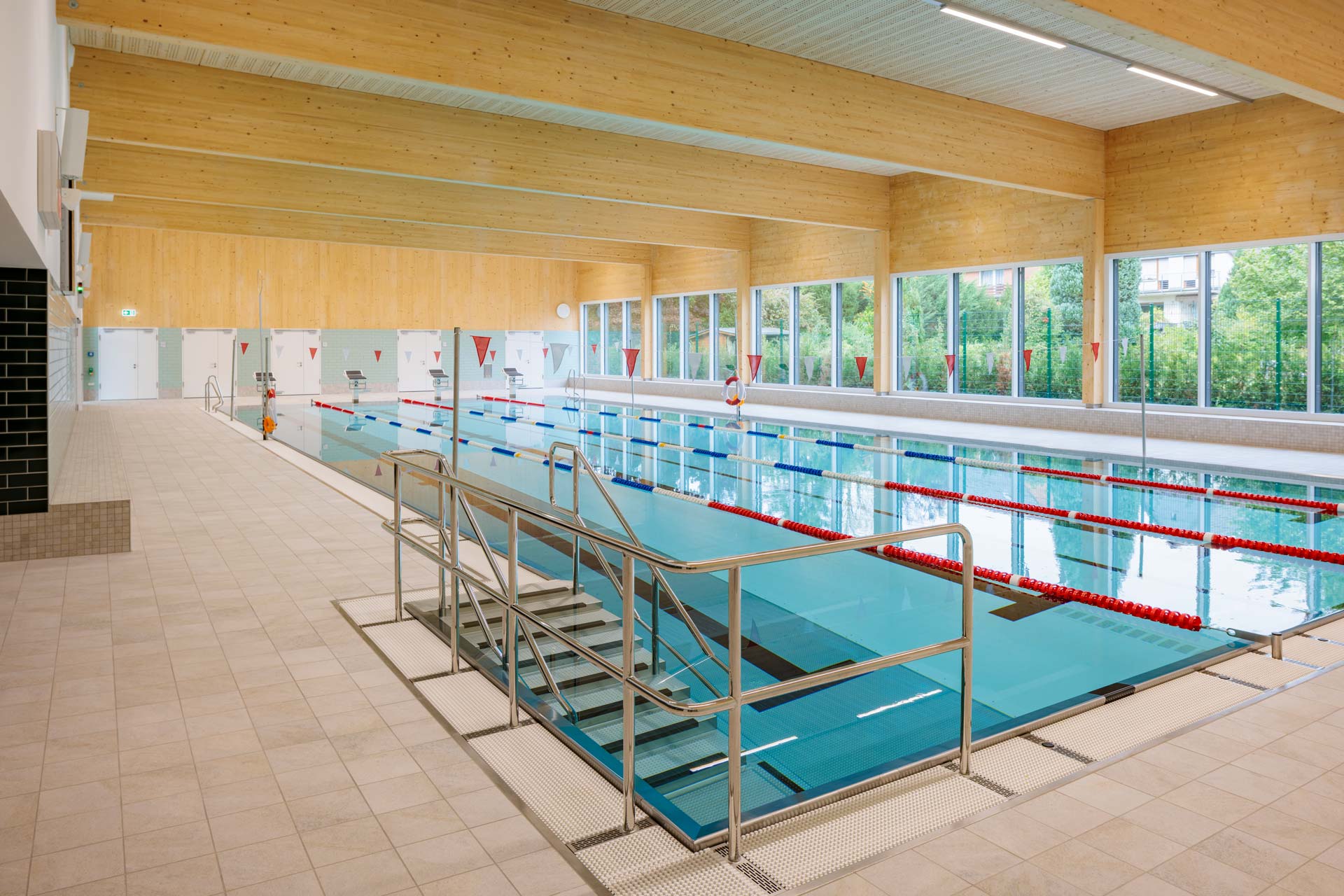Hallenbad mit Treppe als Einstieg, abgetrennten Bahnen und einer umlaufenden Fensterfront.