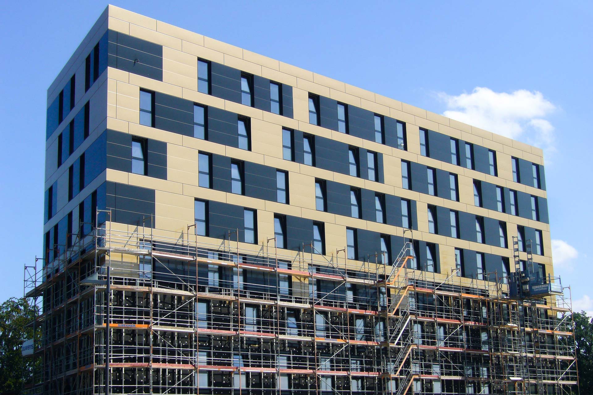 Hochhaus mit hellbrauner und dunkler Fassade, das bis zur H&auml;lfte von einem Bauger&uuml;st verh&uuml;llt ist.