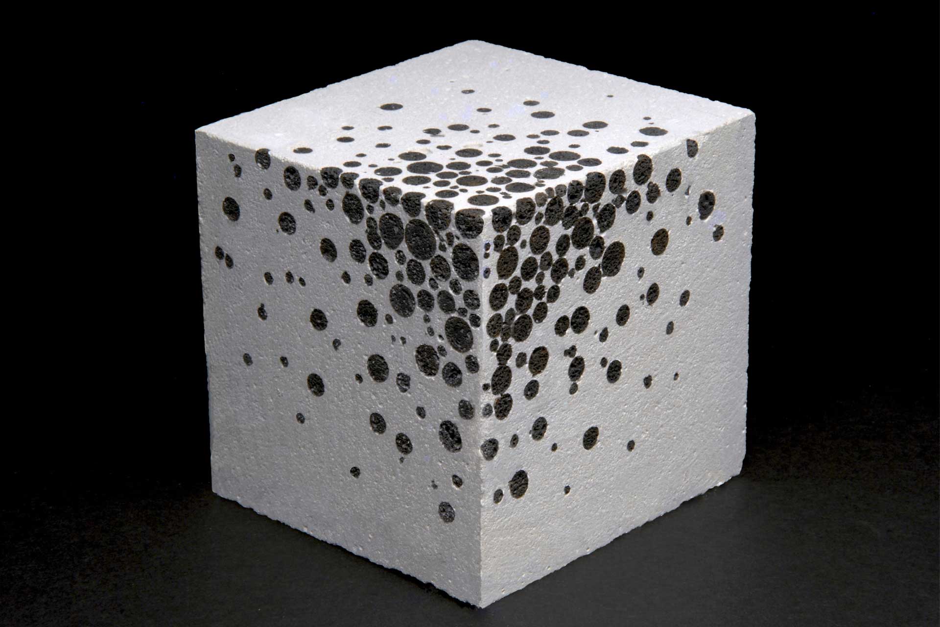 Weißer Betonwürfel mit schwarzen Punkten vor einem schwarzen Hintergrund.