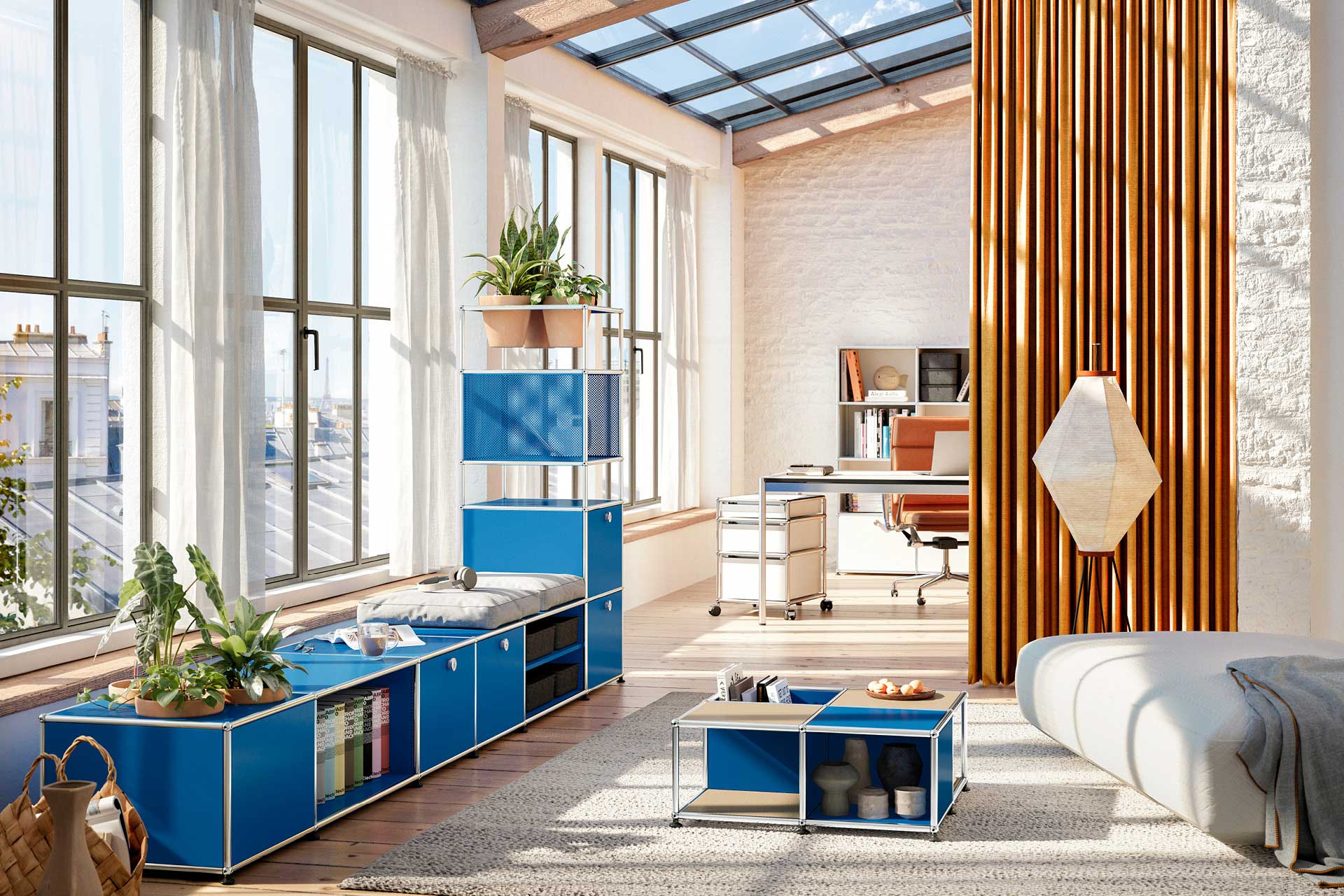 Büroumgebung mit Schreibtisch und Sofa sowie blauen USM Regalen am Fenster.