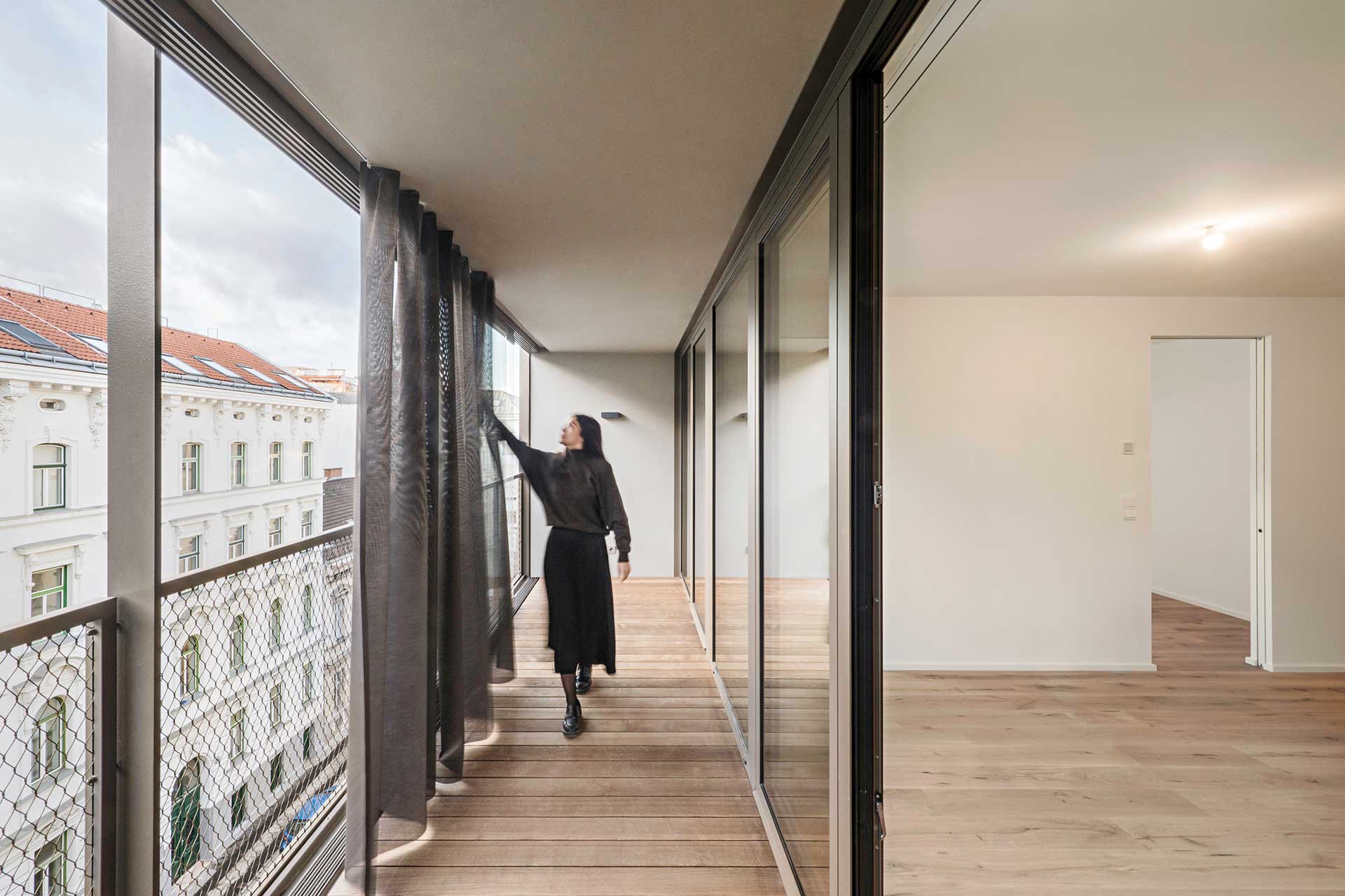 Verglaster Balkon mit Vorhang. Rechts ist ein Zimmer zu erkennen.